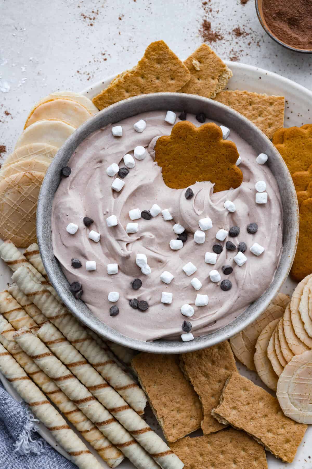 This hot cocoa dip recipe has only 3 ingredients and comes together in 5 minutes. It's chocolatey, fluffy, sweet, and creamy. It's perfect to take to holiday parties or cozy winter gatherings. Overhead shot of hot cocoa mix on a platter with different types on cookies.